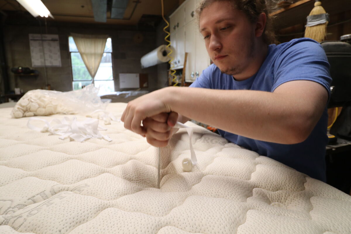 A Beloit bedmaker hand-finishing a mattress top