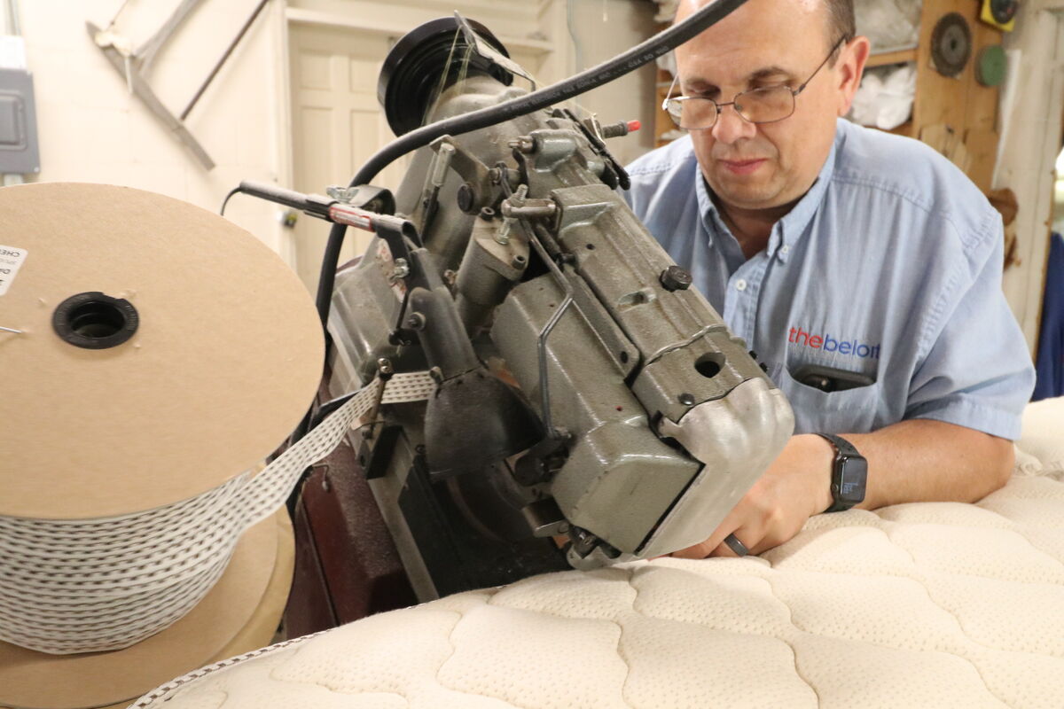 A bedmaker tufting a quilted mattress